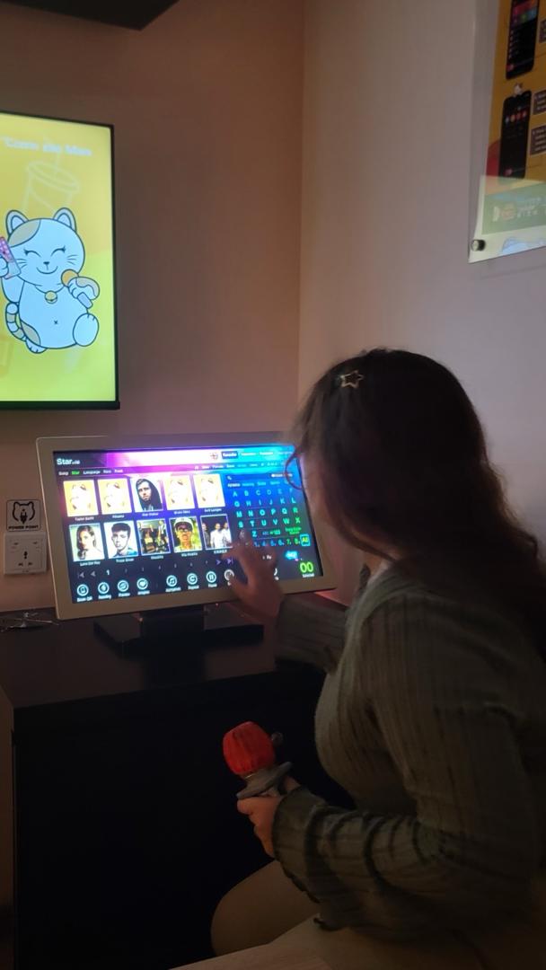 Sera choosing a song during karaoke in her olive outfit